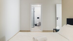 Een moderne hotelkamer met een groot bed, een nachtkastje met een lamp en een deur naar de badkamer.