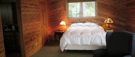 Un dormitorio de cabaña de madera con una cama, dos lámparas de noche, una silla y una ventana.