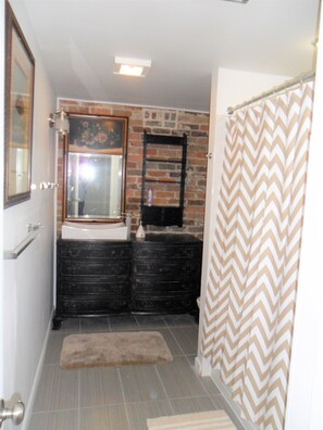 Une salle de bain avec un mur en briques, un miroir, un lavabo, un meuble-lavabo noir et un rideau de douche.