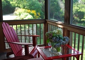Een houten stoel en een glazen tafel met een bloevas op een balkon met uitzicht op groen.