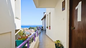 Varanda estreita com vista para o mar e edifícios, plantas em vasos e uma porta de madeira.