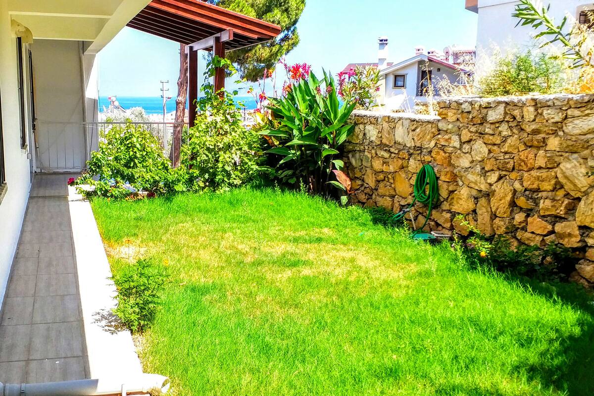 Un jardín bien cuidado con un muro de piedra, un pérgola y vista al mar.