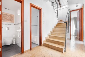 A modern bathroom with a toilet, sink, and shower. A wooden staircase leads to another room. - MAMAD, Penthouse & Jacuzzi in Neve Tzedek by FeelHome (Tel Aviv - Jaffa)
