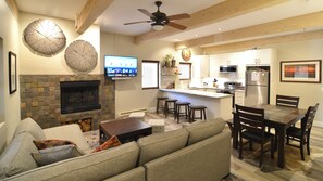 Une cuisine moderne avec une cheminée en pierre, des poutres apparentes en bois au plafond et un coin repas doté d’une grande table et de chaises.