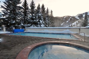 Une piscine dont le bord est recouvert de carrelage, entourée d’un sol et d’arbres couverts de neige.