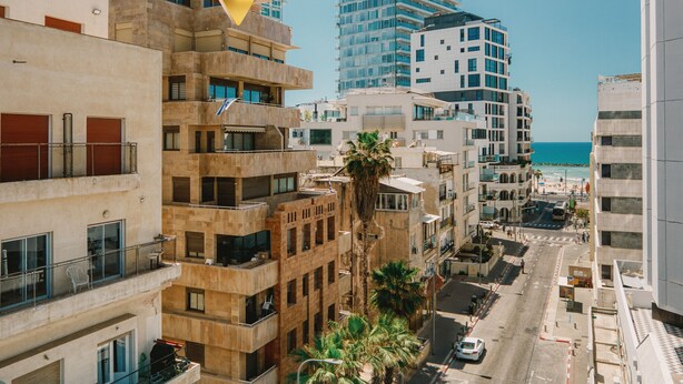 Un immeuble à plusieurs étages doté de balcons, d’un palmier et offrant une vue sur la mer.