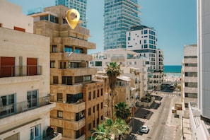 A multi-story building with balconies, a palm tree, and a view of the sea.