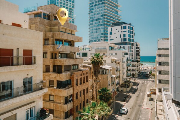 A multi-story building with balconies, a palm tree, and a view of the sea.