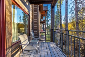 A wooden deck with chairs and a table, overlooking a forested area.