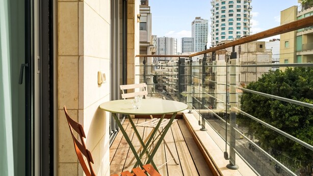 Un balcon doté d’une balustrade en verre, d’une petite table et d’une chaise.