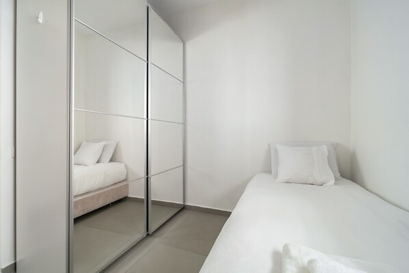 A minimalist bedroom with a bed, a wardrobe, and a mirror.
