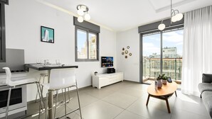 Un appartement moderne comprenant une cuisine, un coin repas et un salon. Il dispose de grandes fenêtres, d’un téléviseur à écran plat et d’un balcon offrant une vue sur la ville.