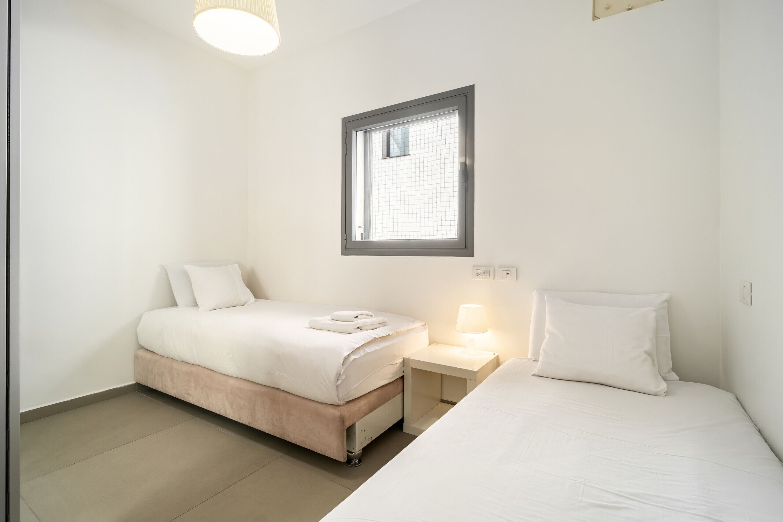 A bedroom with two beds, a window, a nightstand, and a lamp.
