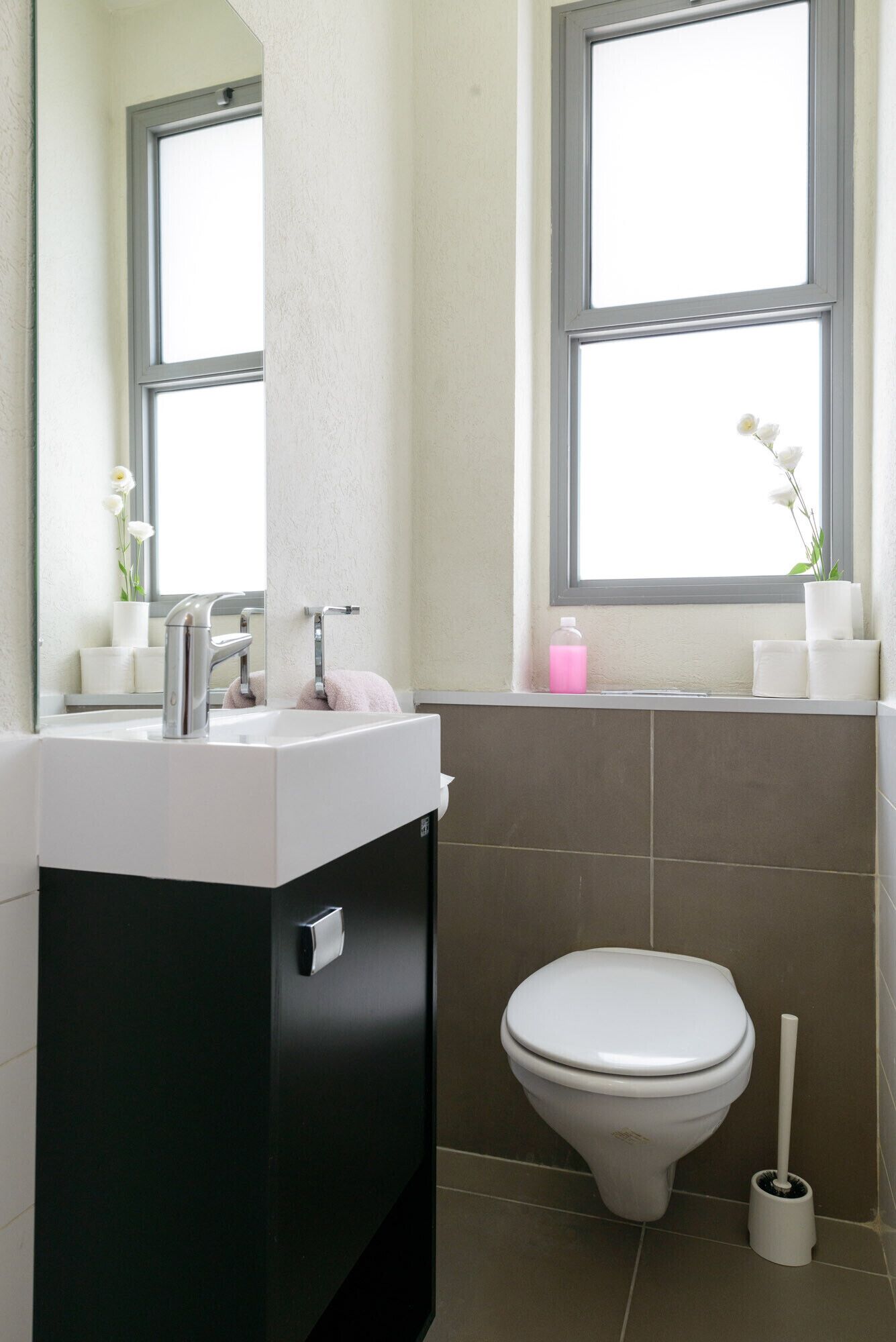 Ein modernes Badezimmer mit einem weißen Waschbecken, einer Toilette und einem Fenster über dem Waschbecken.