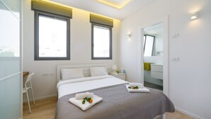 A modern bedroom with a large bed, two windows, a bedside table, and a mirror. - MAMAD Comfort 3BR & Balcony in City Center by FeelHome (Tel Aviv - Jaffa)