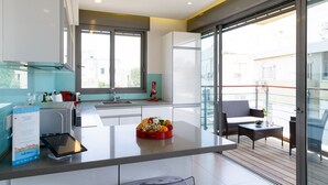 A modern kitchen with a large island, a dining area with a glass table, and a balcony with outdoor seating. - MAMAD Comfort 3BR & Balcony in City Center by FeelHome (Tel Aviv - Jaffa)