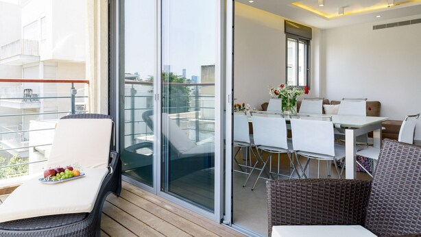 A balcony with a dining table, chairs, and a wicker sofa. - MAMAD Comfort 3BR & Balcony in City Center by FeelHome (Tel Aviv - Jaffa)