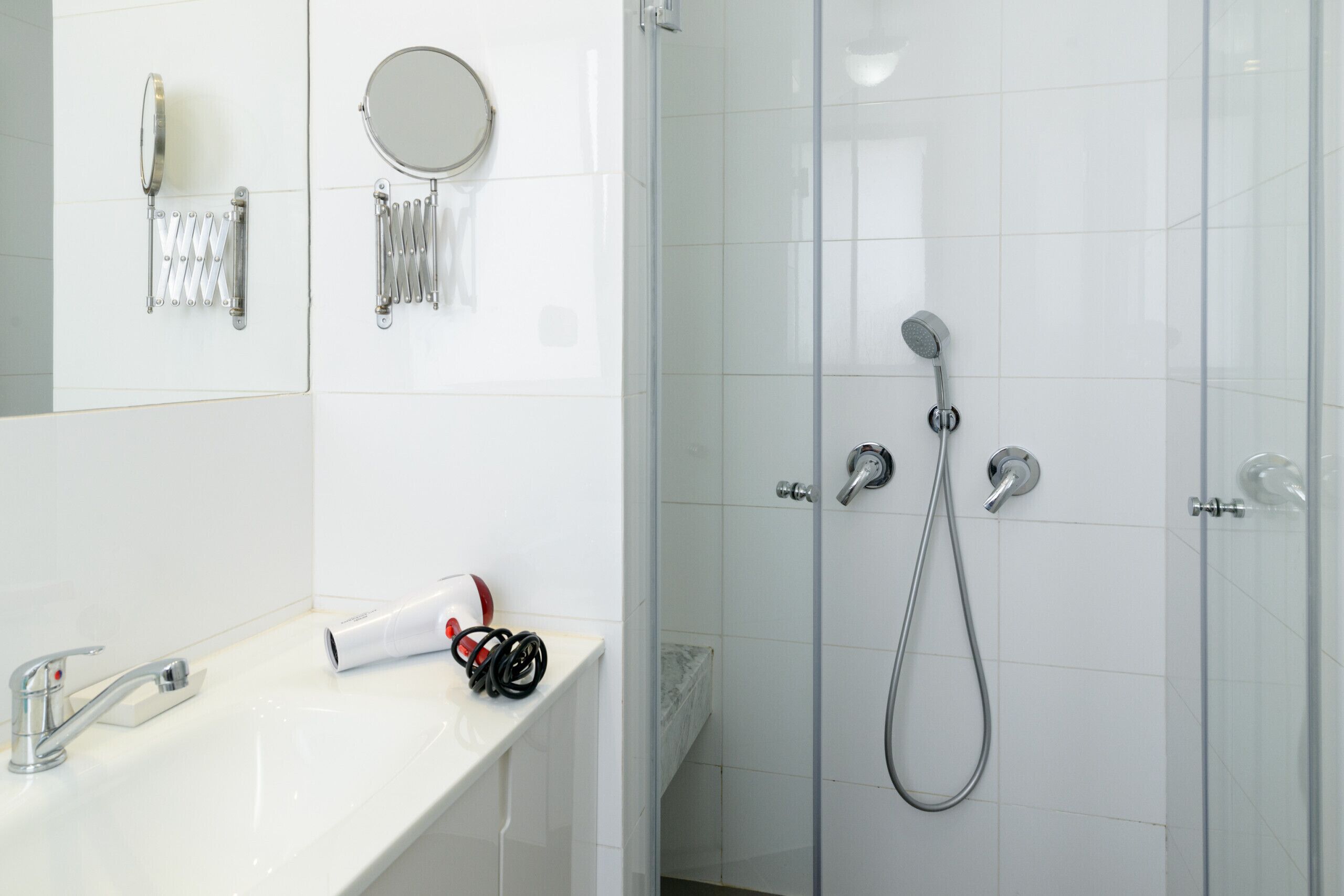 A modern bathroom with a white sink, a handheld showerhead, and a glass-enclosed shower stall.
