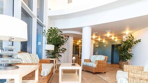 Moderni aula, jossa on rottinkihuonekaluja, suuri valkoinen pöytä keskellä ja ruukkukasveja.