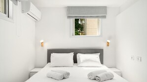 Una habitación de hotel moderna con una cama grande, dos mesitas de noche, un ventanal con vistas y un equipo de aire acondicionado.