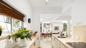 Una cocina moderna con una isla central, un comedor con sillas rojas y vistas al exterior a través de amplias ventanas.