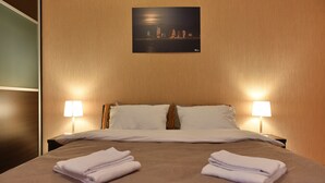 A hotel room with a bed, two bedside lamps, a night view poster, and neatly folded towels on the bed. - Apartment in old Tbilisi (Dzveli Tbilisi)