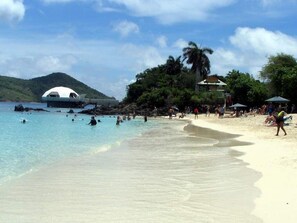 Ein Strand mit klarem Wasser, einer weißen Kuppelstruktur und Menschen beim Schwimmen und Sonnenbaden.