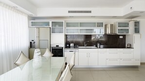 A modern kitchen with white cabinetry, a glass dining table, and a built-in oven. - Penthouse with Terrace & Panoramic View by FeelHome (Tel Aviv - Jaffa)