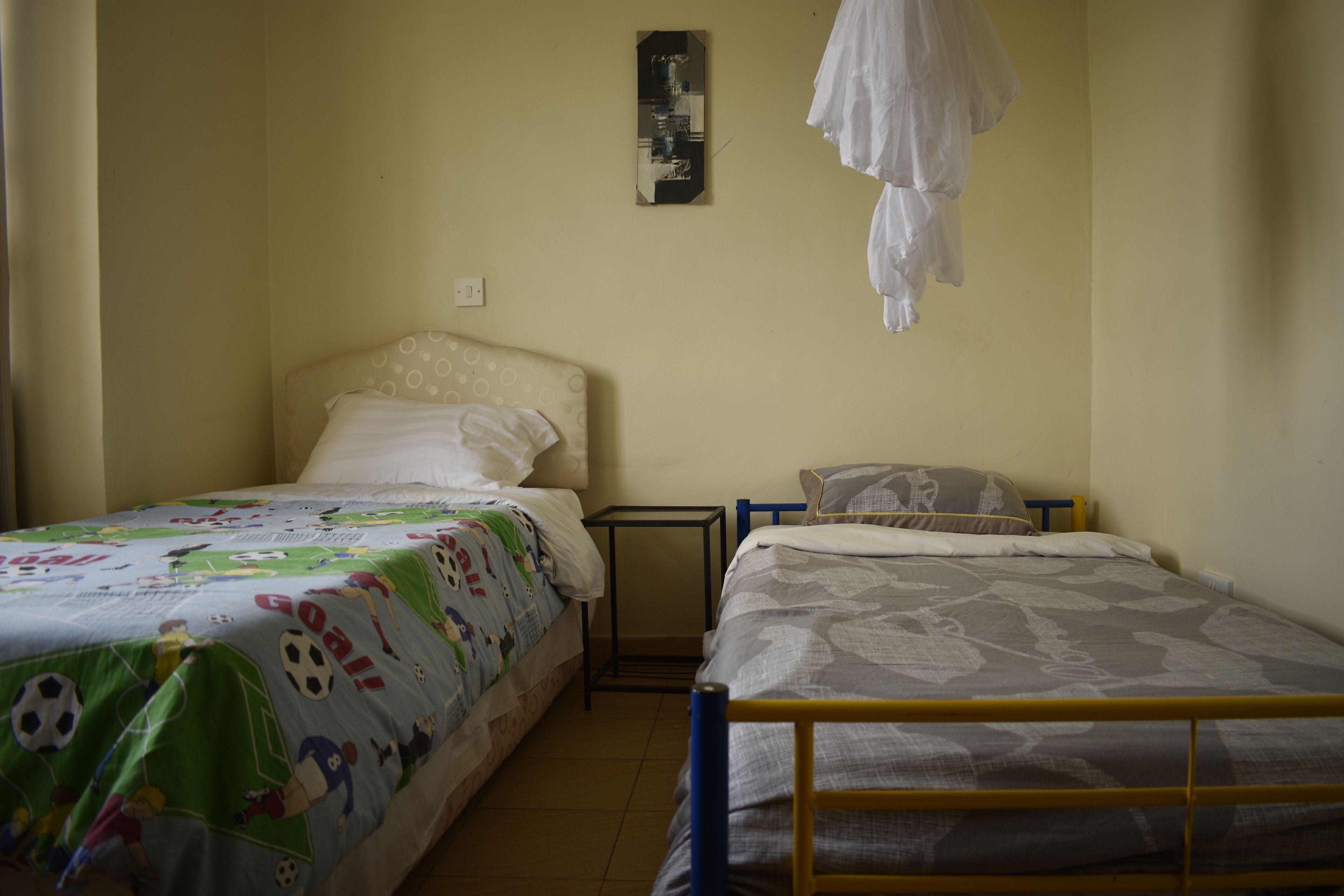 A bedroom with two beds, one with a soccer-themed bedspread and the other with a floral pattern. There is a small table and a hanging light fixture.