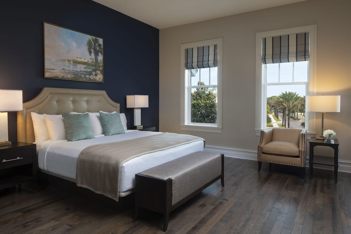 A bedroom with a large bed, two bedside tables with lamps, a bench, and a chair.