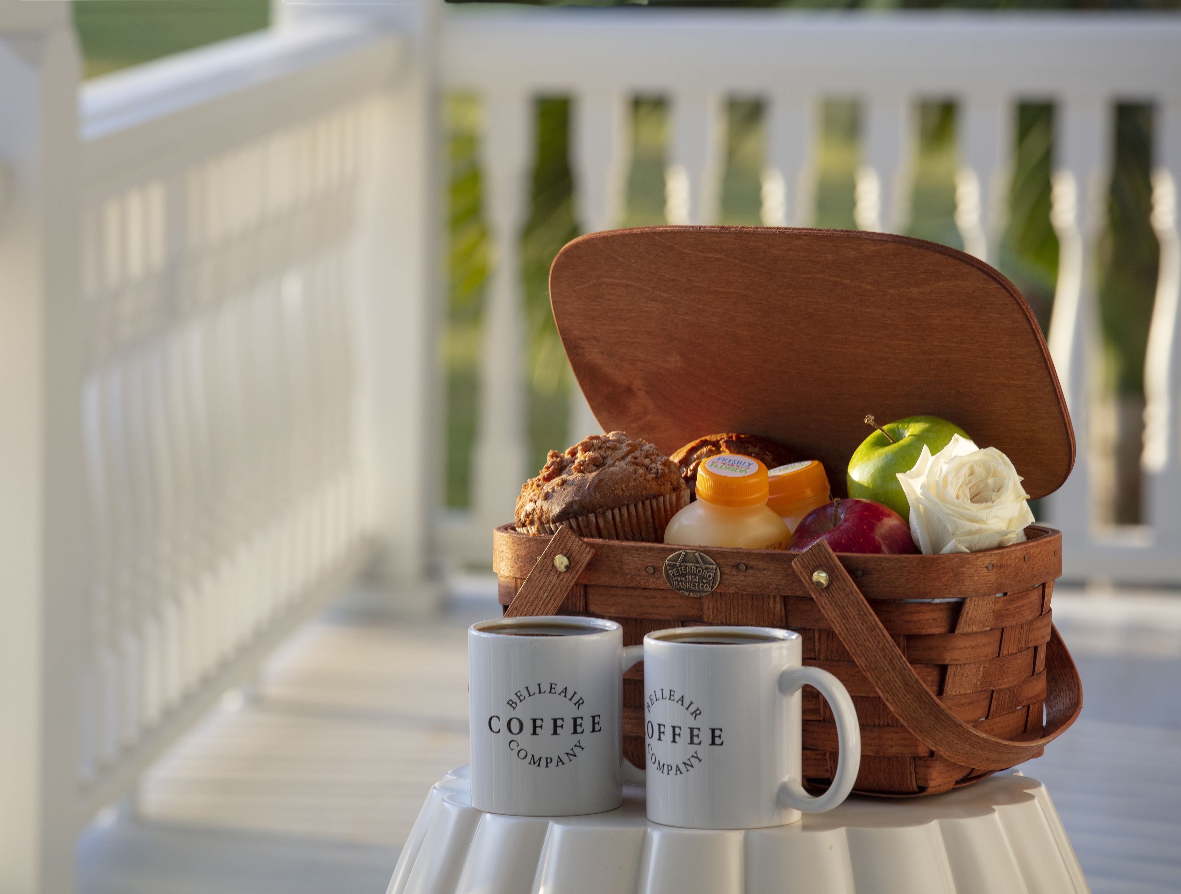 A wooden picnic basket on a white table with two coffee mugs labeled "Belleair Coffee Company".