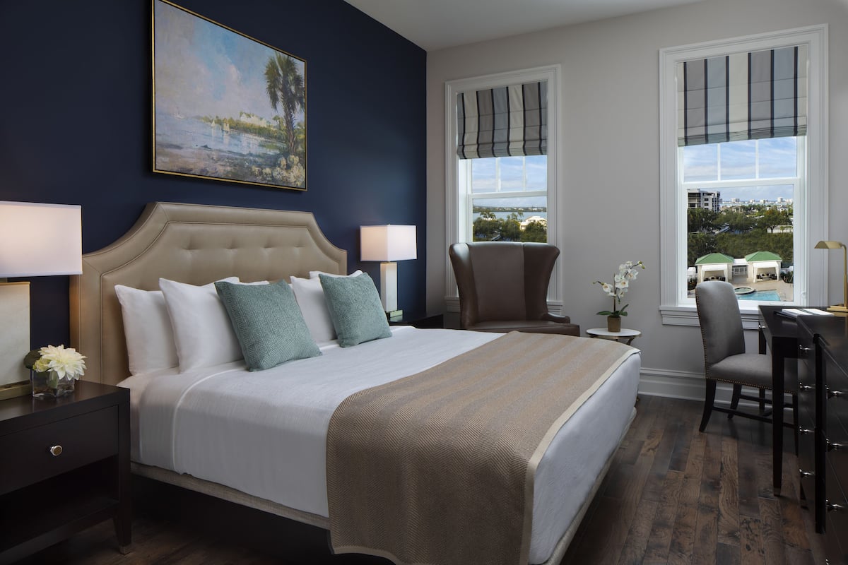 A bedroom with a large bed, two bedside tables, a chair, and a window with a view.