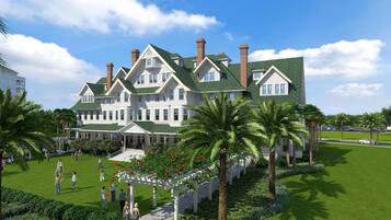 A large, multi-story building with a green roof and white walls, surrounded by a well-maintained lawn and palm trees.