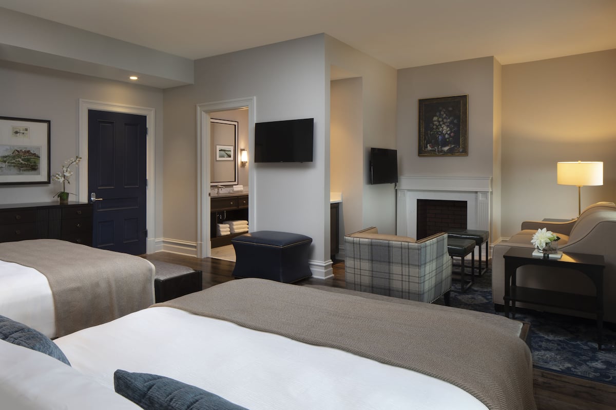 A hotel room with two beds, a sitting area with a fireplace, a television, and a small table with a lamp.