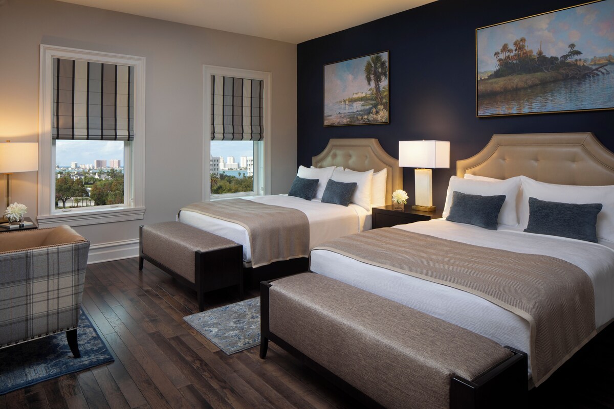 A hotel room with two beds, a view of the city, and artwork on the walls.