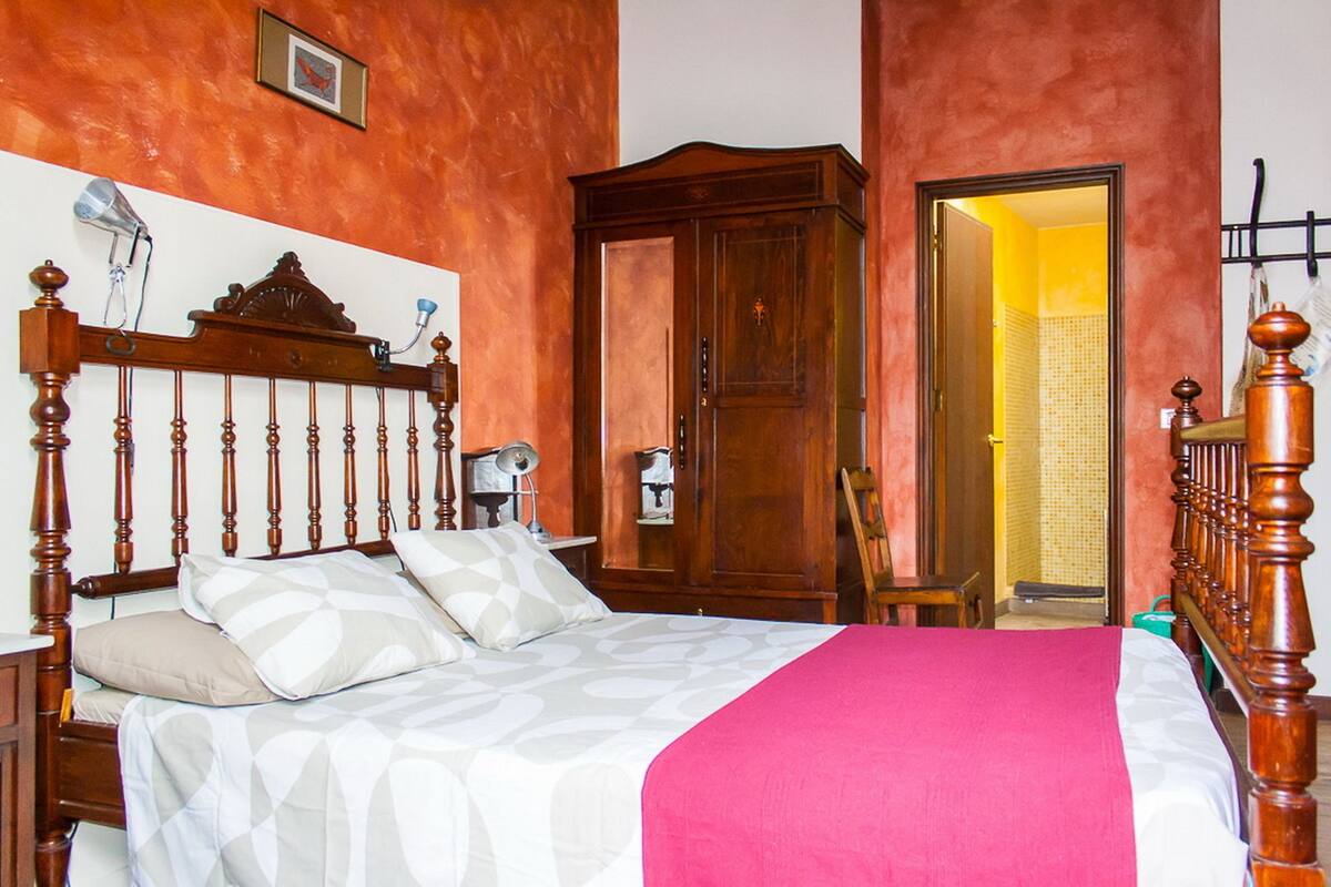 A bedroom with a wooden bed, a wardrobe, and a door leading to another room.
