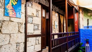 A stone building with a wooden balcony, a colorful painting on the wall, and a small statue on the right. - Casa Luna (Agaete)