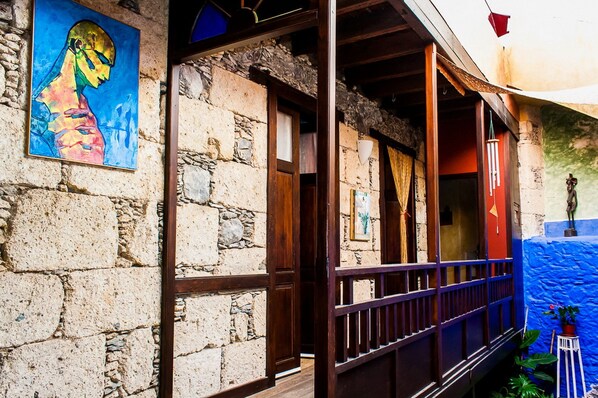 A stone building with a wooden balcony, a colorful painting on the wall, and a small statue on the right. - Casa Luna (Agaete)