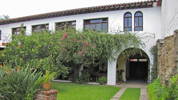 A white building with a tiled roof, a brick pathway, and a well-maintained garden with various plants and flowers.