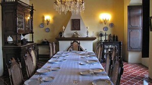 A dining room with a long table set for a meal, a chandelier, and wall-mounted sconces.