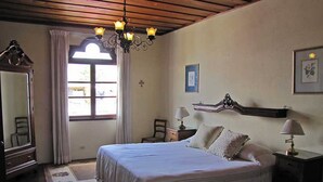 A bedroom with a large bed, a chandelier, a dresser, a mirror, and a window with curtains.