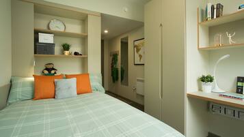 A bedroom with a bed, pillows, a clock, a shelf with books, a globe, and a desk with a lamp.