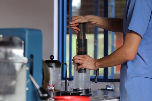A person assembling a cylindrical device with a handle, possibly a vacuum cleaner, on a table with a blue container and a red object nearby. - Finca Temática Cafetera Las Mercedes (Tibacuy)