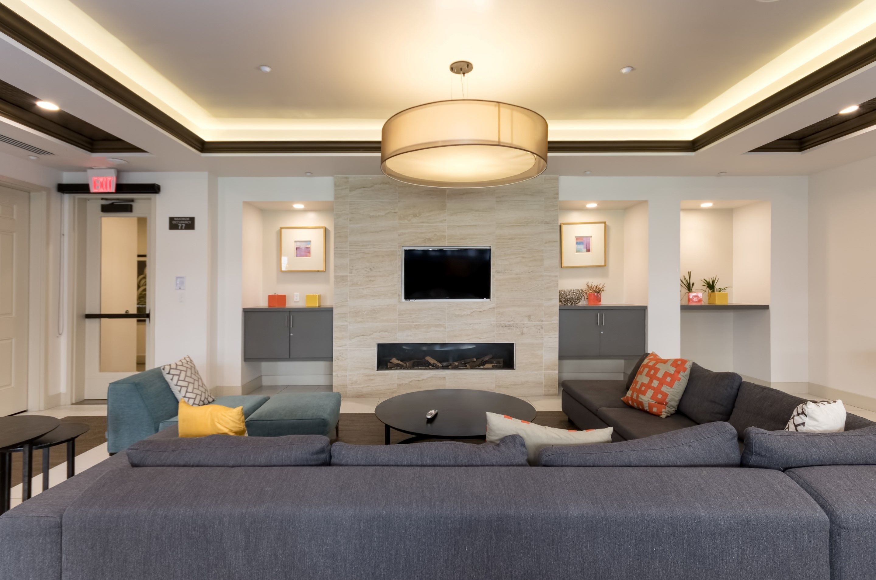 A modern living room with a large sectional sofa, a round coffee table, and a flat-screen TV mounted on the wall.