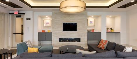 A modern living room with a large sectional sofa, a round coffee table, and a flat-screen TV mounted on the wall.