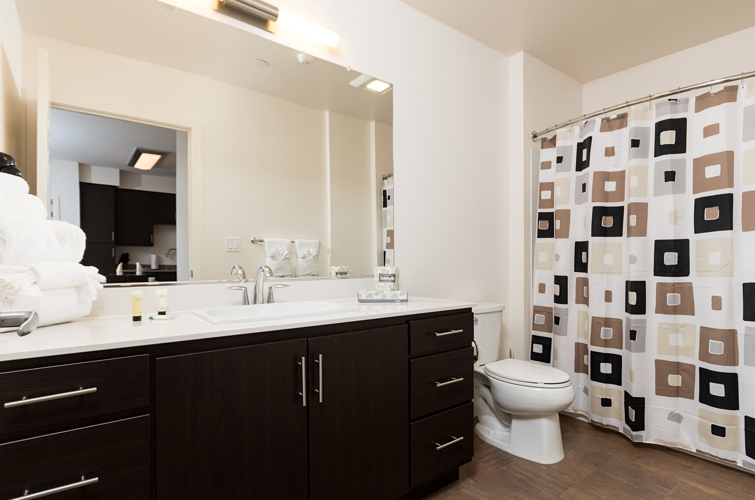 Une salle de bain moderne avec un meuble-lavabo en bois foncé, un grand miroir, des toilettes et un rideau de douche à motifs géométriques.