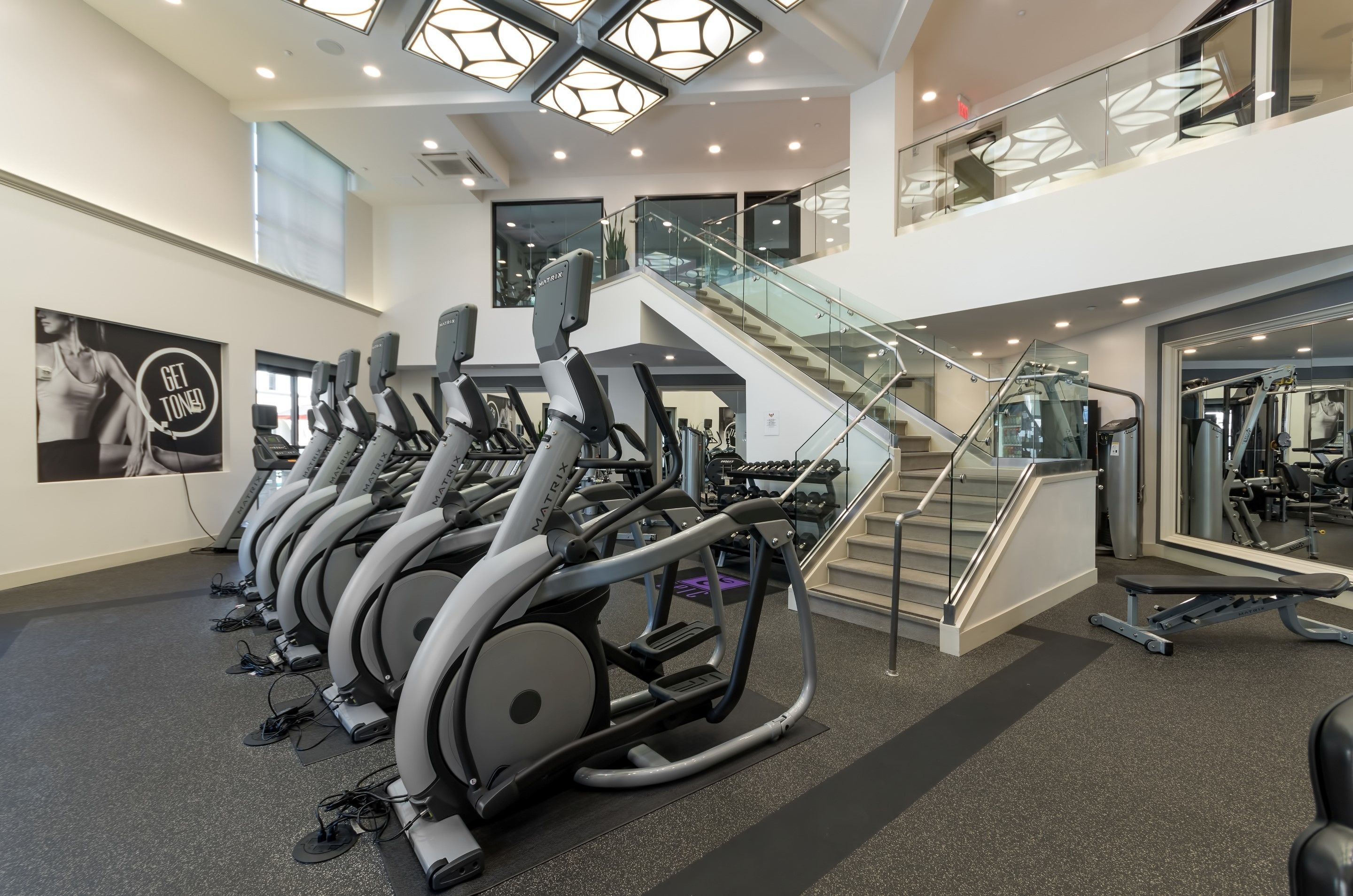 A modern gym with multiple treadmills, a staircase, and a glass railing.