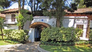 A building with a tiled roof, a stone pathway leading to an arched entrance, and a well-maintained garden with various shrubs. - Casita Jazmin (Antigua Guatemala)