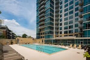 Um hotel moderno com piscina, vários andares e céu claro.