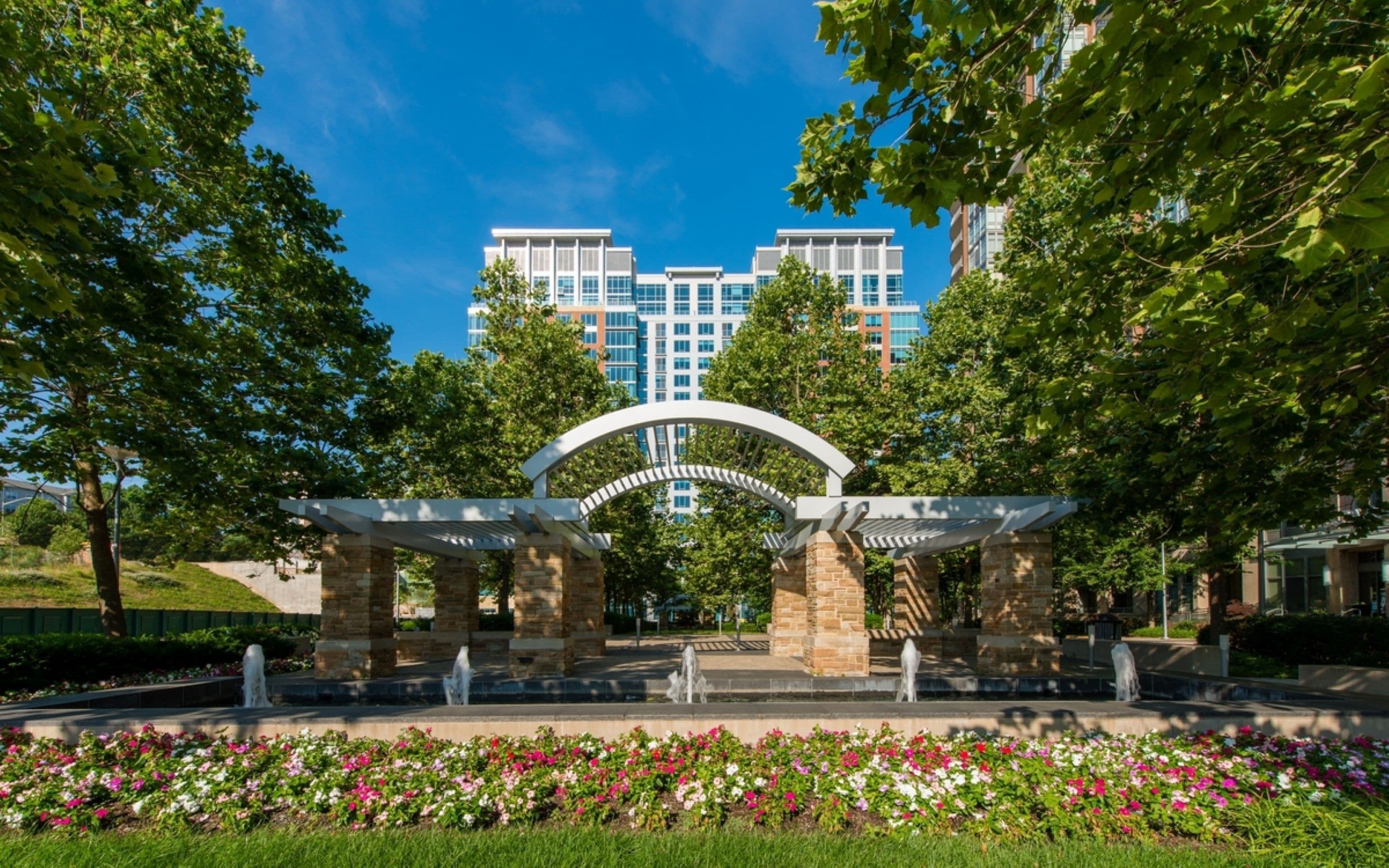 A landscaped entrance with a stone archway, a fountain, and a flower bed.